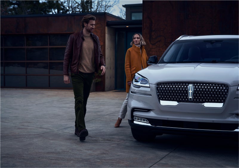 A man and a woman approaching a 2023 Lincoln Aviator® SUV, which illuminates certain lights when they are close | Rydell Lincoln in Independence IA